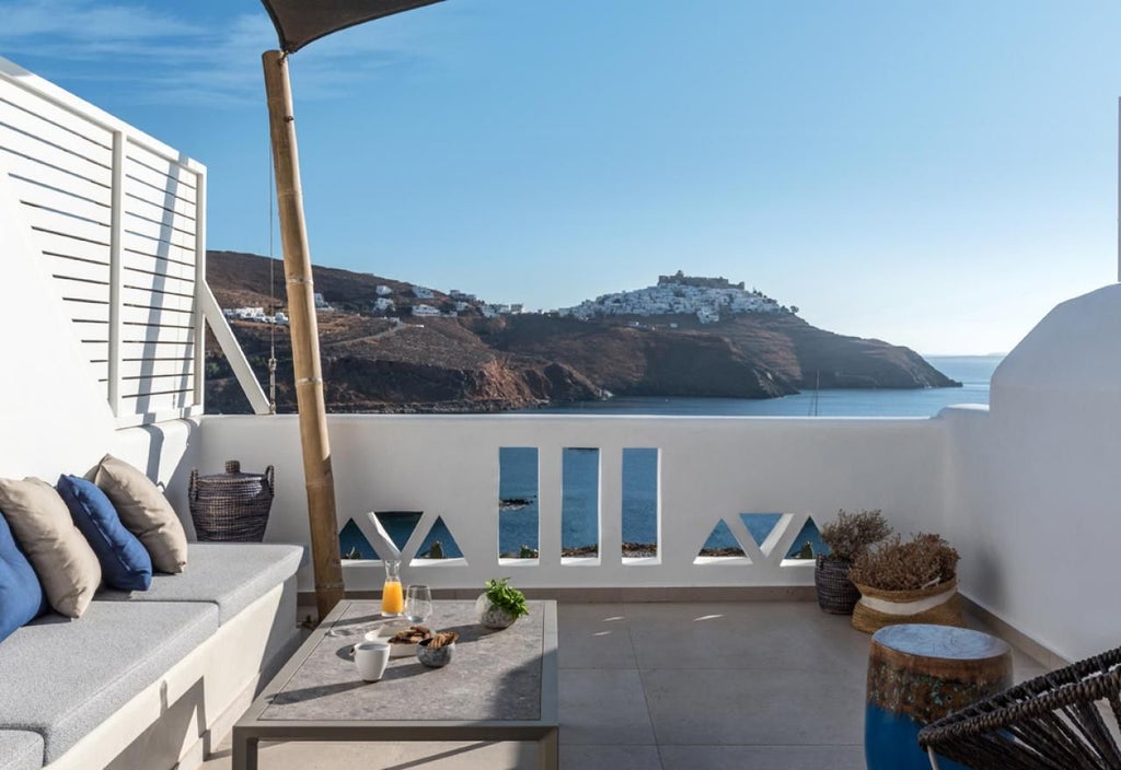 Elegant honeymoon suite in Greece with white minimalist design, luxurious four-poster bed, and stunning Aegean Sea panoramic view through large windows