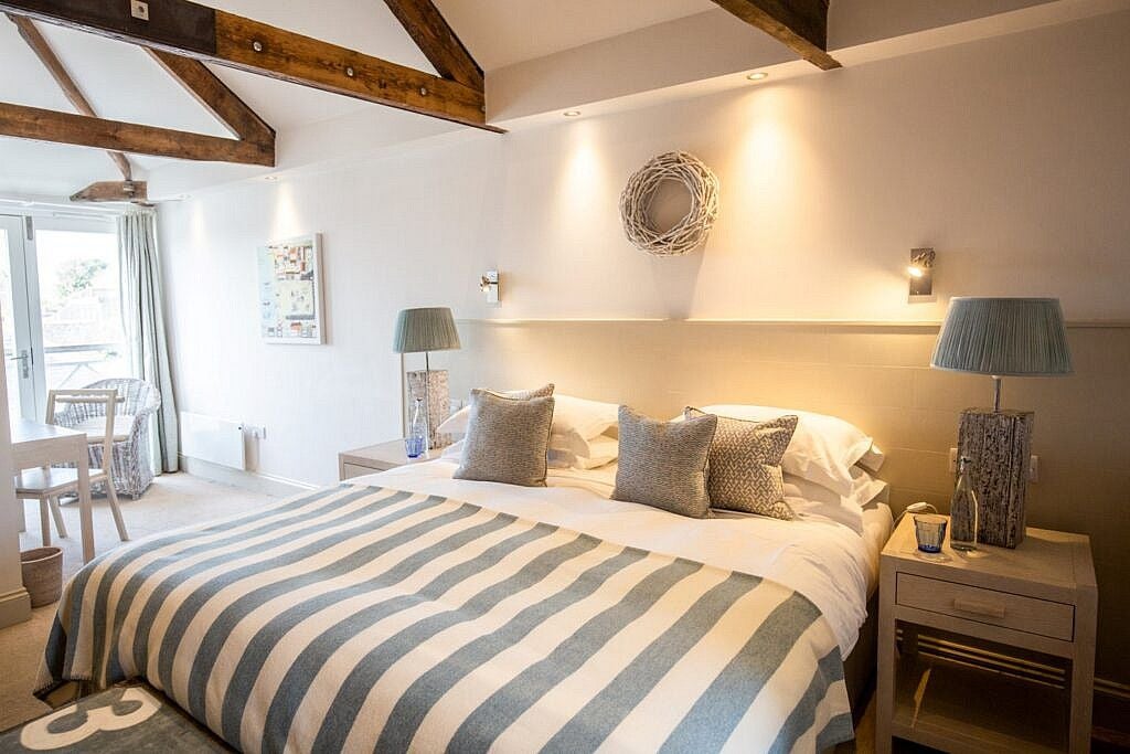 Elegant coastal hotel room with crisp white linens, nautical blue accents, large windows overlooking scenic St Mawes harbor in Cornwall, UK