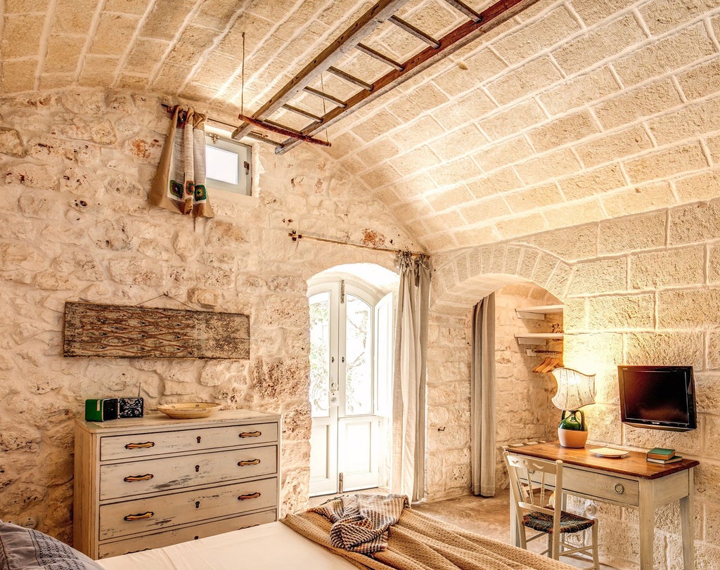 Rustic stone walls, elegant white linens, and soft natural light illuminate a luxurious classic room at Masseria Cervarolo in rural Puglia, Italy.