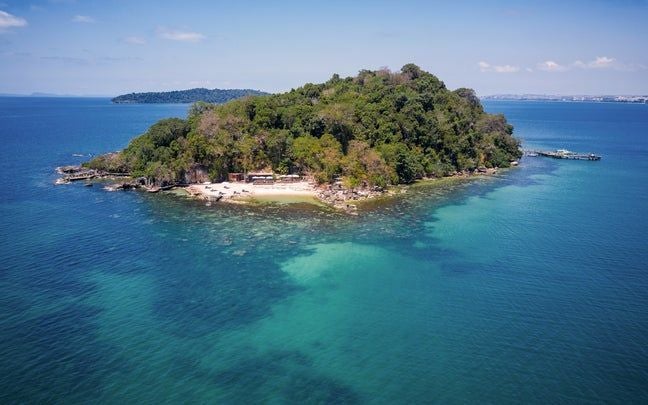 Luxury beachfront villa with infinity pool overlooking turquoise waters and lush tropical forest on private Cambodian island at sunset.