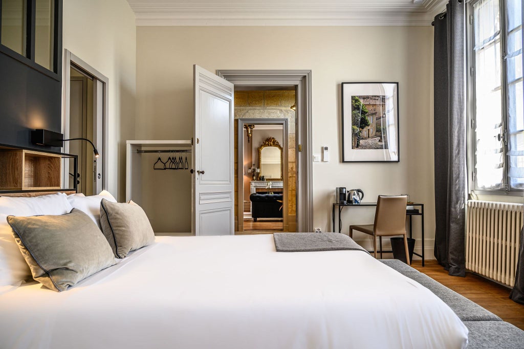 Elegant double room with soft neutral tones, plush white bedding, sophisticated artwork, and classic French architectural details in a luxurious boutique hotel setting