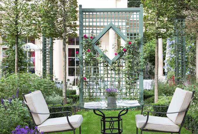 Le Bristol hotel exterior showcases elegant Parisian architecture with cream limestone facade, ornate balconies and manicured topiaries flanking entrance