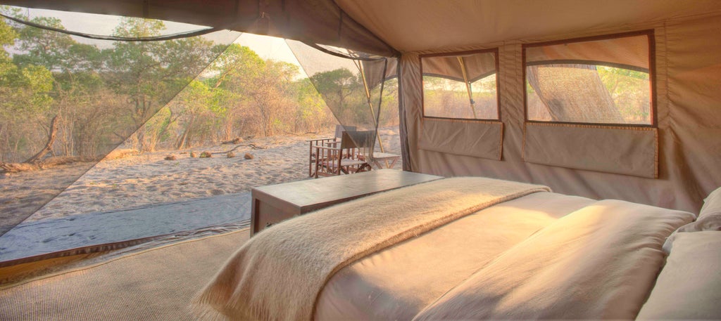 African luxury safari camp with elegant canvas tents nestled among acacia trees, overlooking a golden savanna at sunset in Savute, Botswana