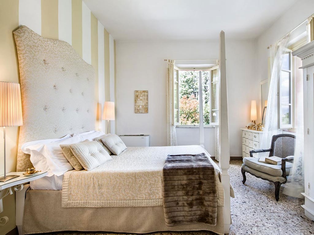 Luxurious Superior Room at Villa Fontelunga, Tuscany, with elegant white linens, soft natural light, and rustic wooden furniture against warm terracotta walls