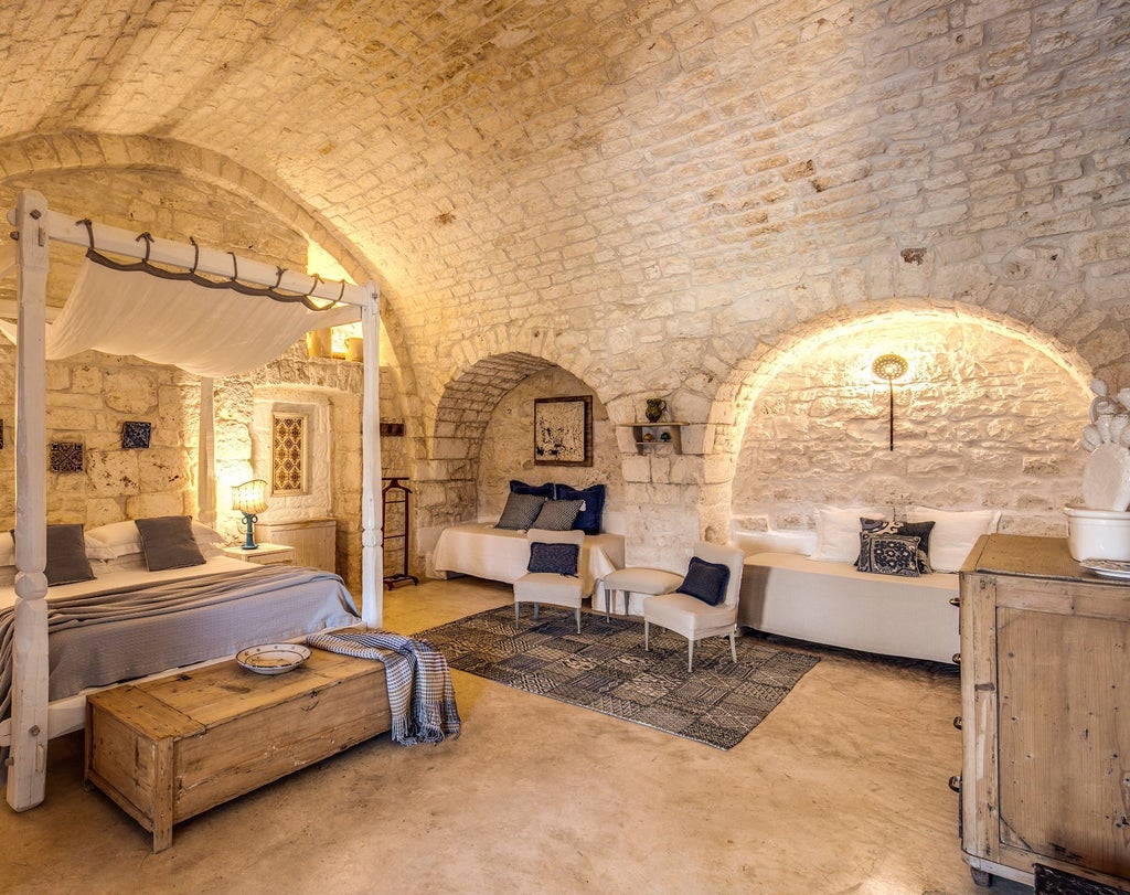 Rustic-chic junior suite with stone walls, elegant wooden furnishings, plush white bedding, and soft natural light in a traditional Italian masseria.