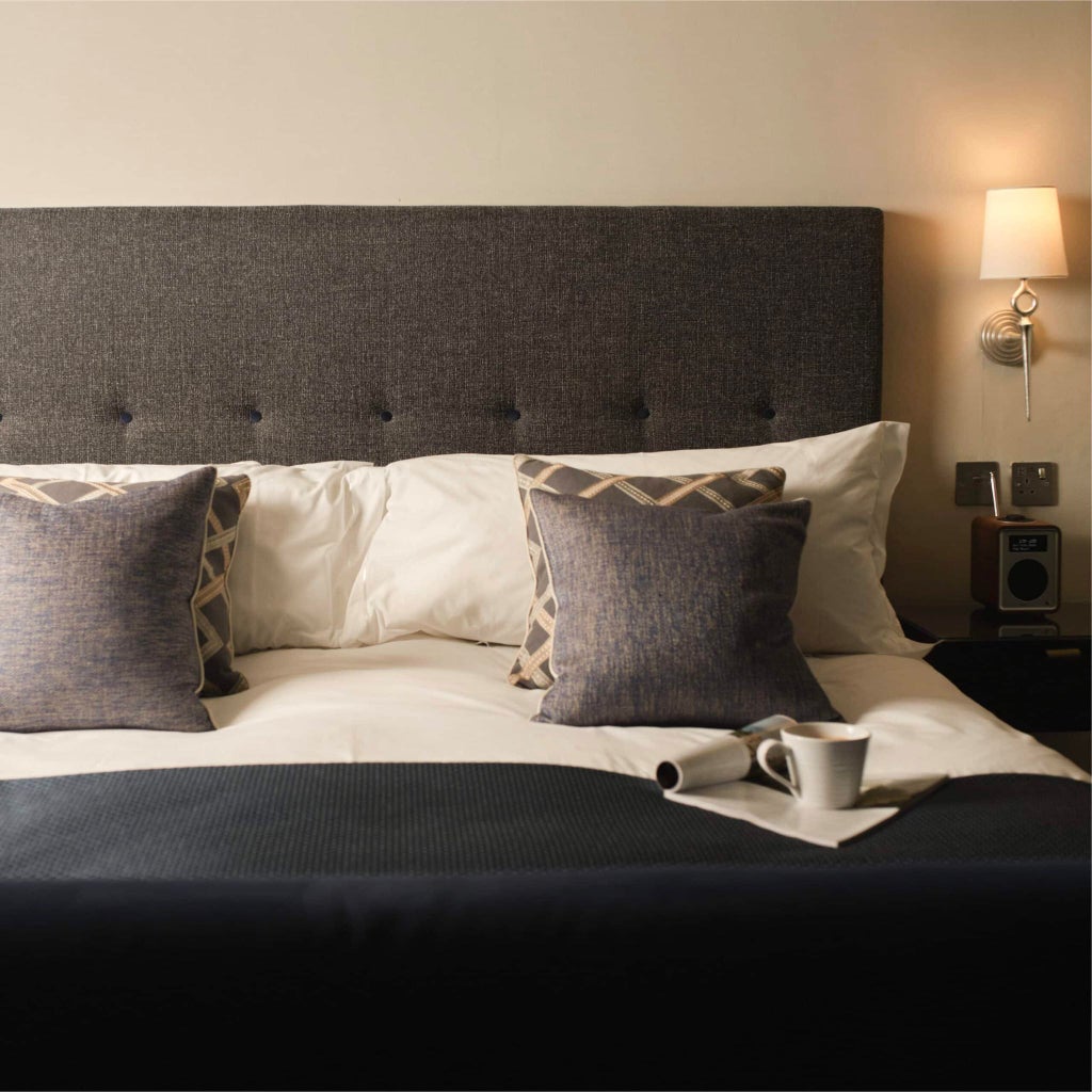 Elegant superior hotel room with plush cream-colored furnishings, crisp white bedding, contemporary artwork, and warm ambient lighting in a luxurious UK accommodation.