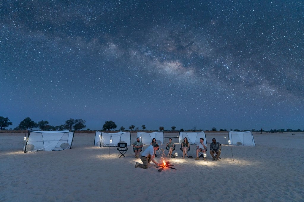 Luxurious wilderness safari lodge nestled along a river, with canvas tents, wooden decking, and lush green landscape in remote Zambian national park
