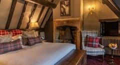 Elegant historic Tudor-style hotel suite with rich wooden furnishings, plush bedding, and classic British decor in warm, inviting tones