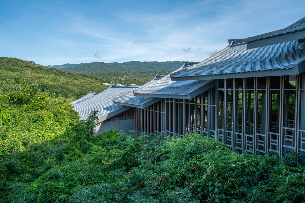 Infinity pool overlooking pristine bay with mountainous coastline, surrounded by elegant pavilions nestled in lush Vietnamese landscape