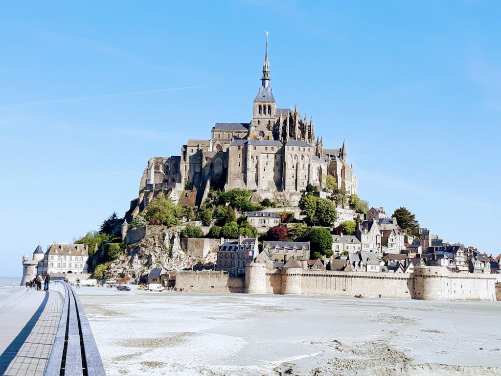 Historic monastery perched on rocky island with dramatic stone bridges, surrounded by turquoise waters and medieval architecture