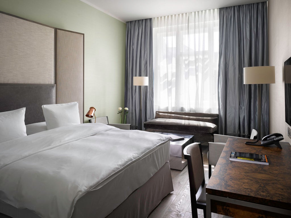 Elegant contemporary suite with plush king bed, dark gray textured walls, modern minimalist furniture, and city view in luxury Scenset Prague hotel room