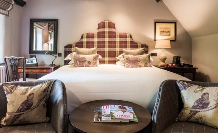 Elegant classic hotel room with plush king bed, antique wooden furnishings, soft neutral color palette, traditional British countryside charm at The Lygon Arms