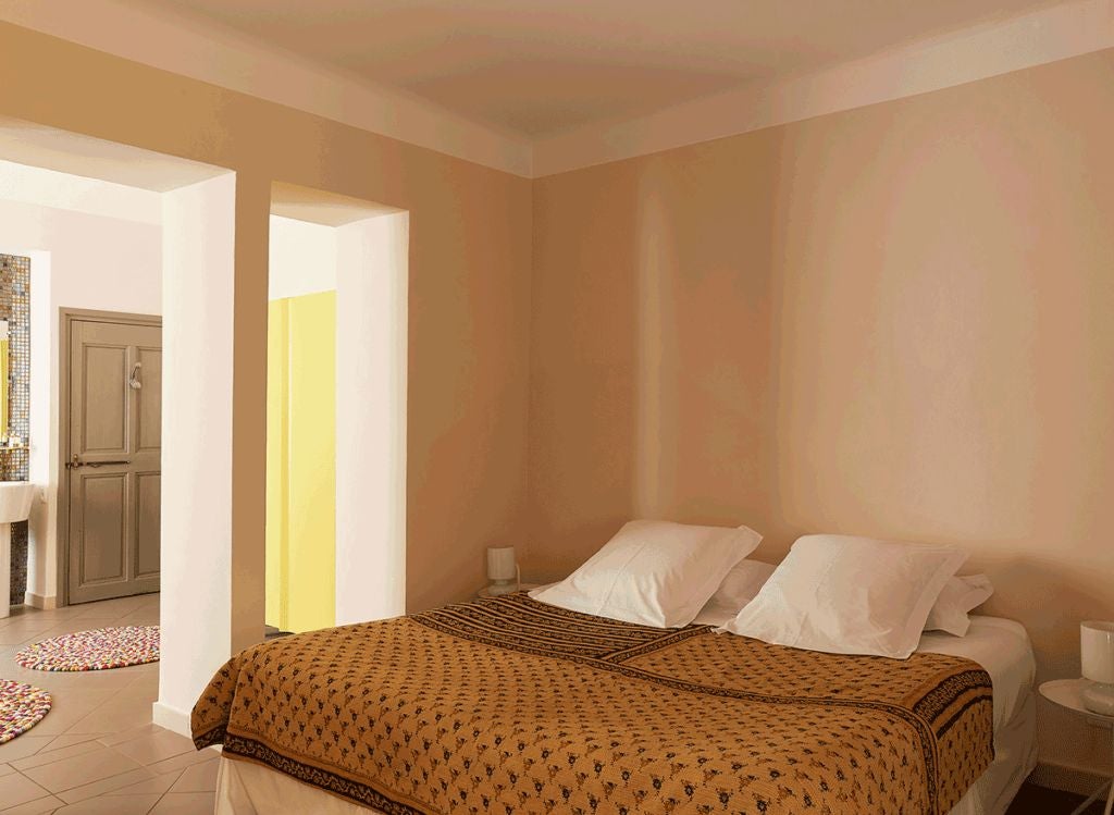 Elegant stone-walled bedroom with luxurious white linens, antique furnishings, and soft natural light streaming through rustic French windows in Provençal hotel