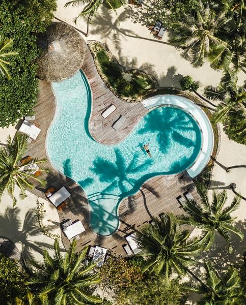 Luxurious overwater bungalows with thatched roofs stretching into crystal-clear turquoise lagoon against Mount Otemanu backdrop at sunset