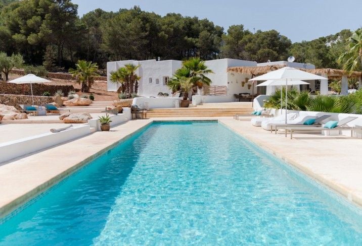 Modern white Mediterranean villa with infinity pool overlooking Ibiza coastline, featuring minimalist design and luxurious outdoor lounge area