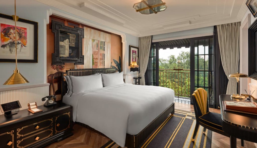 Elegant hotel suite with French colonial decor, featuring a plush king bed, gold-trimmed headboard, and vintage-inspired art deco lamps