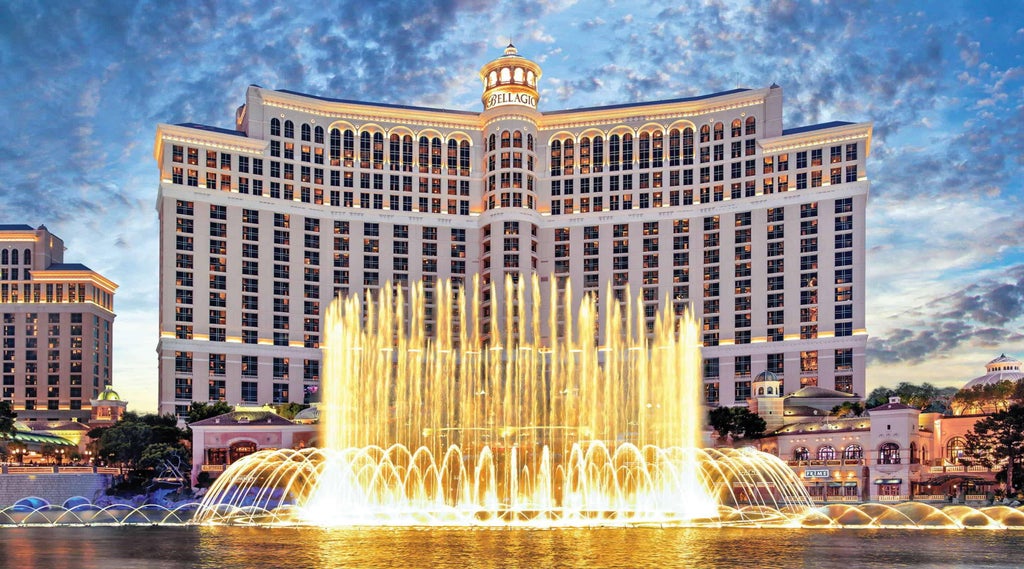 Majestic Bellagio Hotel's iconic Mediterranean-style facade reflects in its famous dancing fountains against the Las Vegas night sky