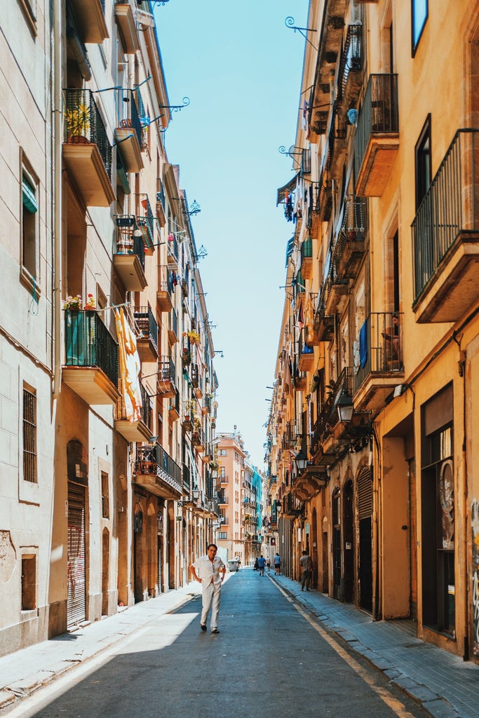 Historic Barcelona street with ornate Gothic architecture, wrought-iron balconies, and cobblestone path leading to majestic cathedral spires