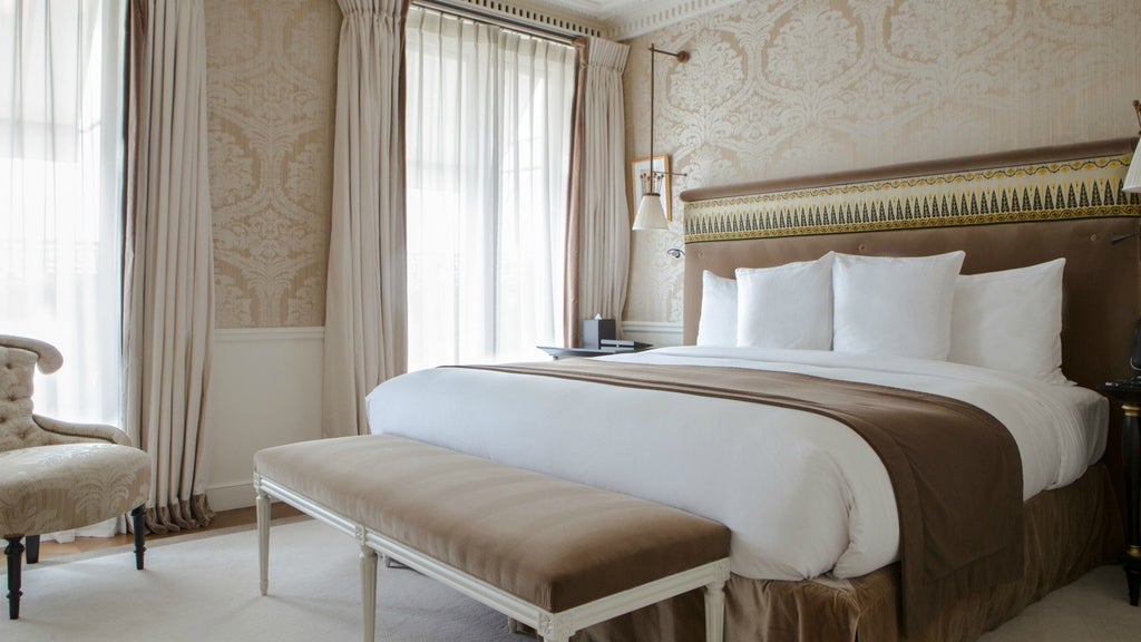 Elegant Parisian hotel suite with panoramic city view, plush cream-colored furnishings, ornate chandelier, and luxurious gold-toned accents overlooking Grand Palais