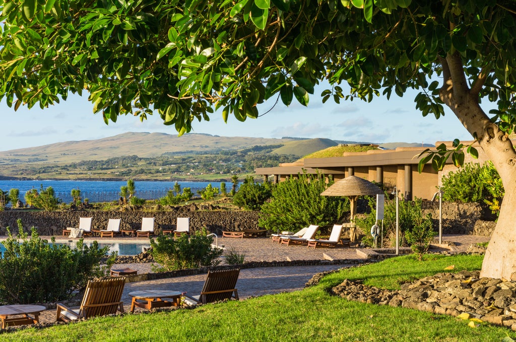 Modern beachfront resort on Easter Island with curved grass-covered roofs, stone walls, and panoramic ocean views at sunset