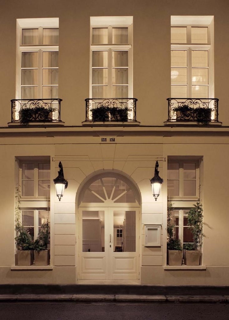 Elegant beige and gold facade of Château Voltaire hotel in Paris, featuring ornate windows, wrought-iron balconies, and classic French architectural details