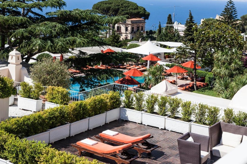 White stone luxury Mediterranean hotel with arched windows, palm trees and elegant outdoor terrace overlooking the Bay of Naples at sunset