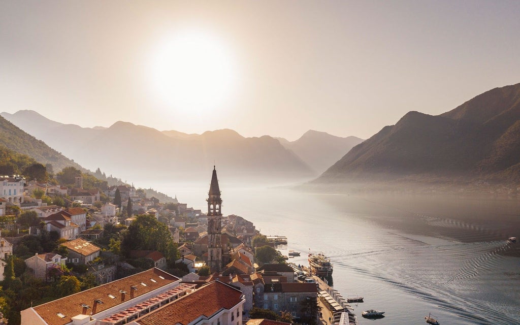 Luxurious sailboat gliding through Montenegro's Bay of Kotor, with dramatic limestone cliffs and historic coastal town framing azure Adriatic waters