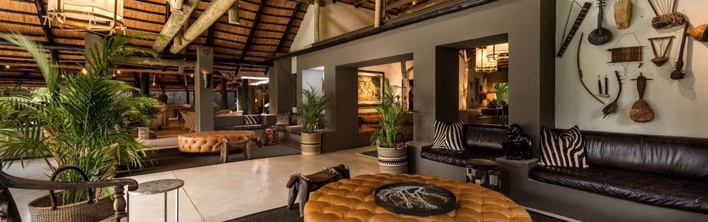 Luxurious safari lodge with thatched roof overlooking a tranquil waterhole, surrounded by African bush vegetation at sunset