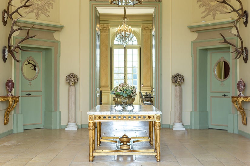 Elegant 18th-century French château hotel with grand limestone facade, symmetrical architecture, and manicured gardens at golden hour