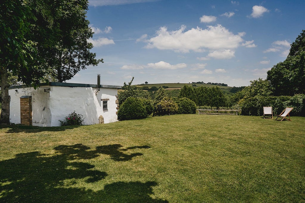 Rustic stone farmhouse hotel nestled in lush Devon countryside, featuring traditional Dartmoor architecture with slate roof and weathered stone walls