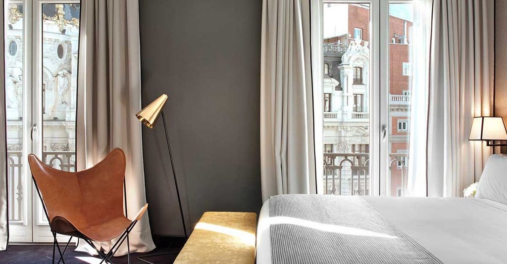 Luxurious deluxe hotel room in Madrid with elegant modern decor, floor-to-ceiling windows offering stunning panoramic city skyline views and sophisticated design elements