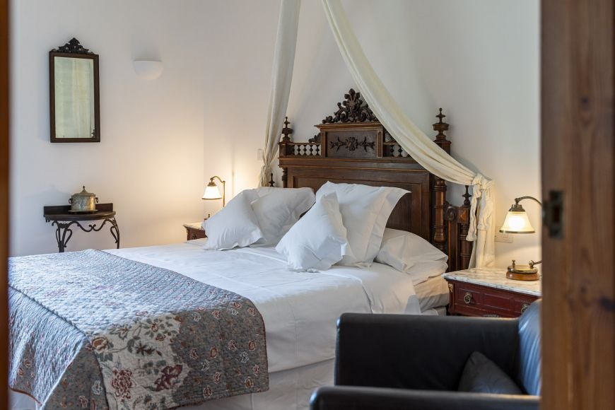 Elegant Mediterranean-style bedroom with white linens, rustic wooden furniture, and soft natural light at Ca's Xorc Luxury Retreat in scenic Spain