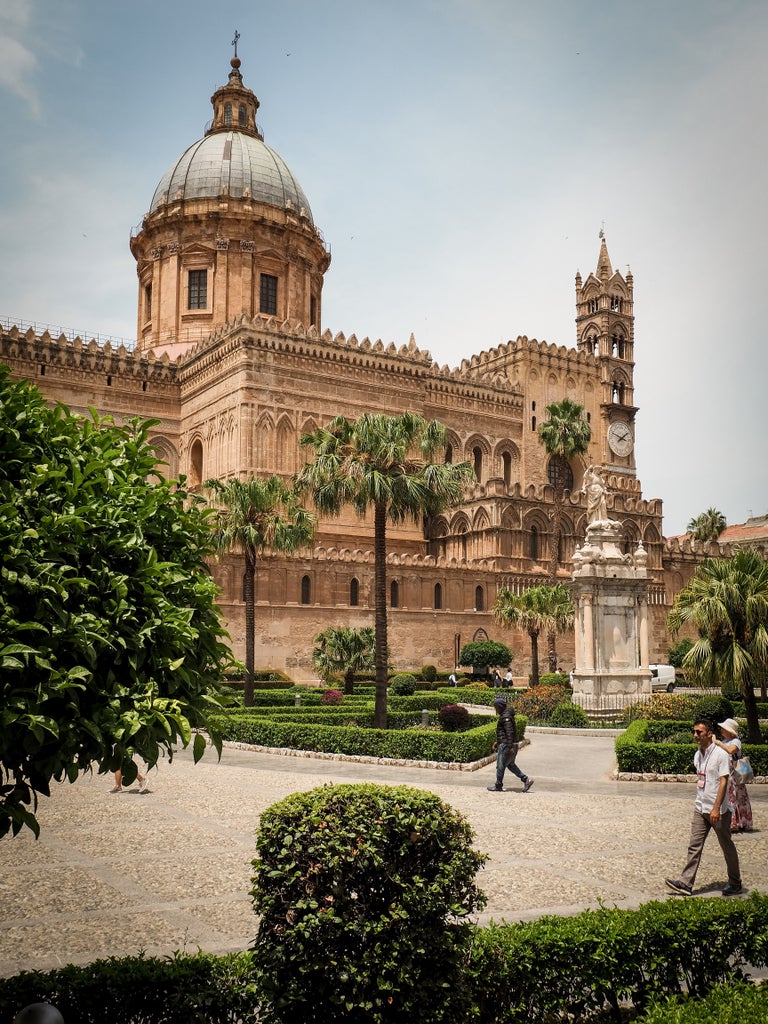 Historical baroque architecture along narrow cobblestone street in Palermo, Sicily, with ornate balconies and golden sunlight