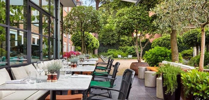 Historic Amsterdam canal house hotel with elegant brick facade, arched windows, and ivy-covered walls reflecting in tranquil waters at sunset