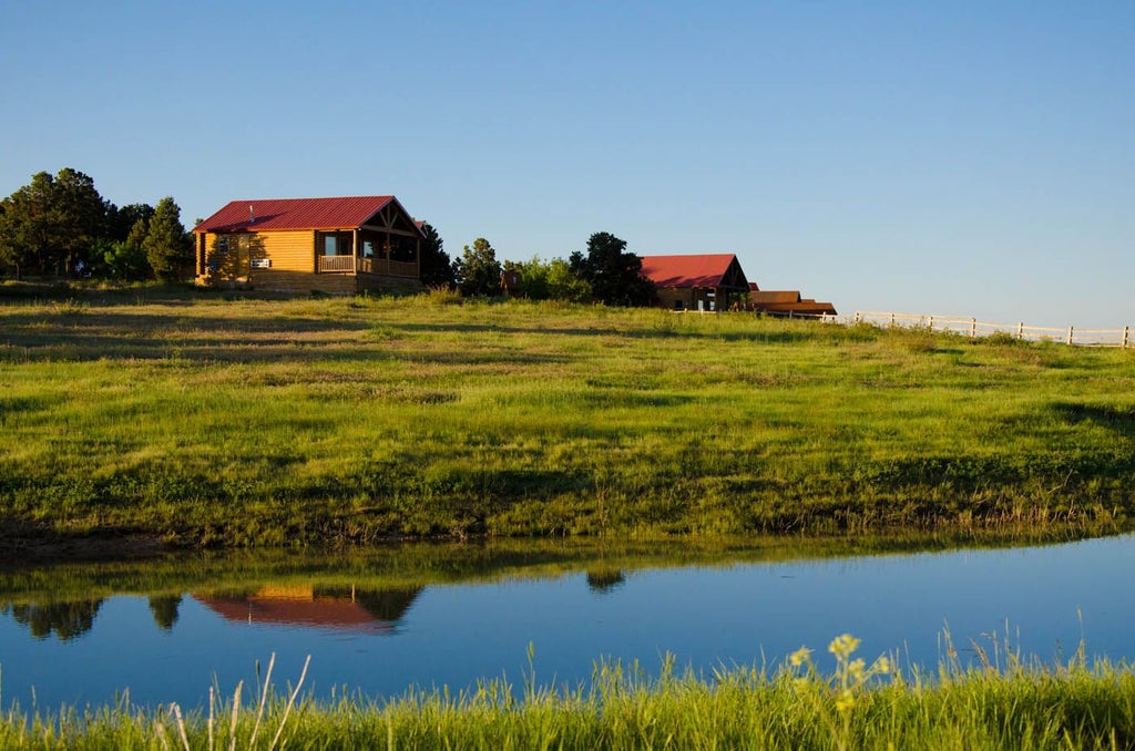 Rustic wood-paneled luxury cabin suite with plush king bed, large windows overlooking scenic mountain landscape in scenset Ranch, United States.