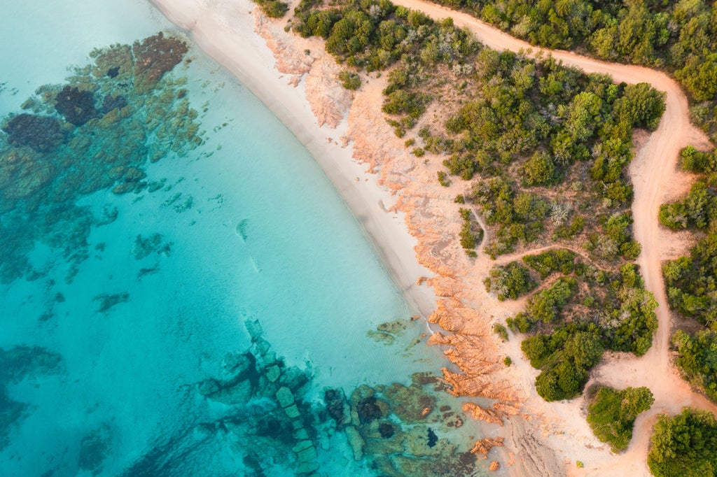 Luxurious wooden yacht sailing along turquoise waters of Costa Smeralda, passing dramatic cliffs and exclusive Mediterranean villas