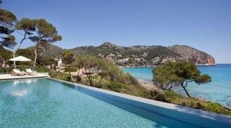 Luxurious Mediterranean coastal hotel with stone walls, nestled on a rocky cliff overlooking turquoise waters near Cala Ratjada, Mallorca