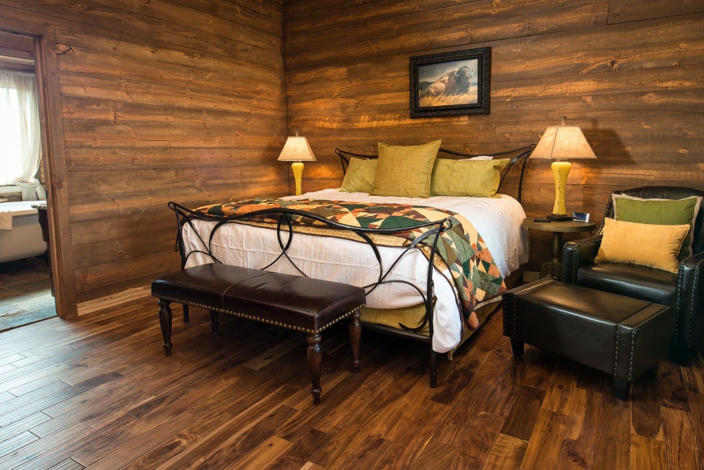 Rustic wooden lodge interior with king-sized bed, large windows overlooking scenic mountain landscape at Scenset Mountain Ranch in southwestern United States.