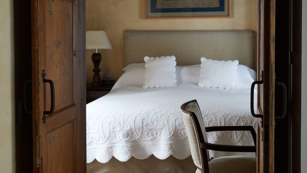 Elegant Spanish hotel room with high beamed ceiling, marble bathroom, antique furnishings, and plush king bed with crisp white linens.