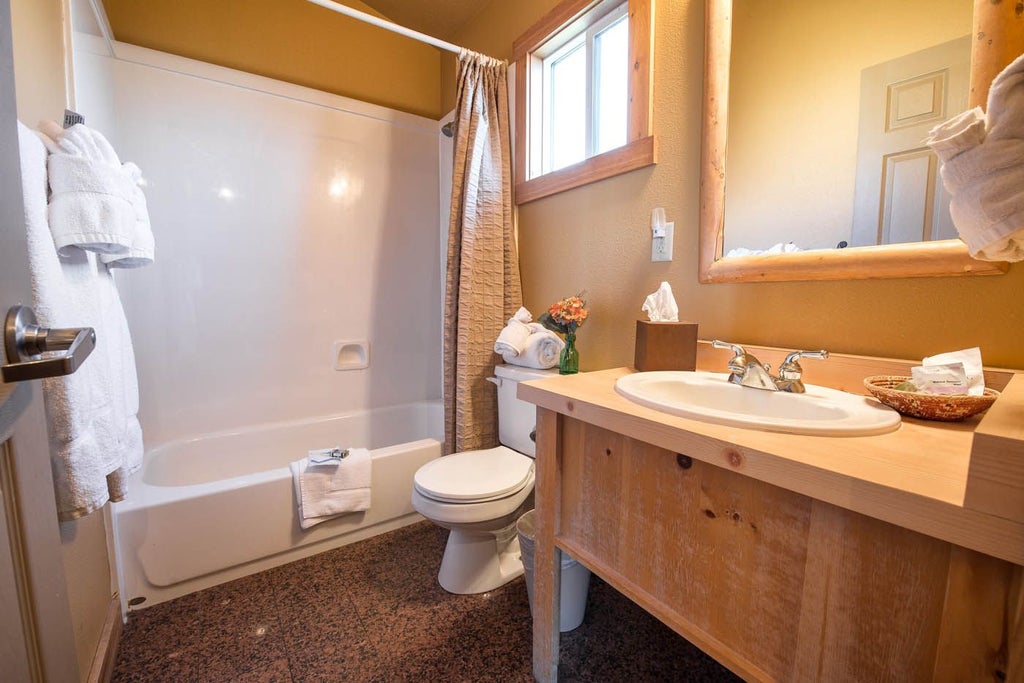 Rustic wooden cabin interior at Scenset Mountain Ranch, featuring warm earth tones, plush bedding, and panoramic mountain landscape through large windows.