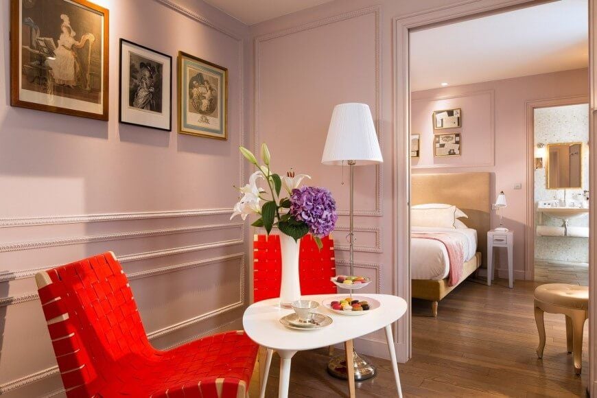 Elegant Parisian hotel room with soft pink walls, luxurious king bed, plush textiles, and vintage-inspired decor reflecting romantic French design aesthetic