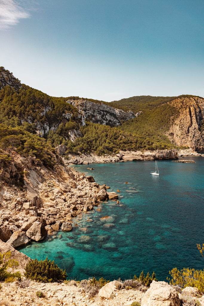 Tranquil aerial view of Ibiza's white-sand beach with turquoise Mediterranean waters, luxury yachts, and clifftop villas at sunset