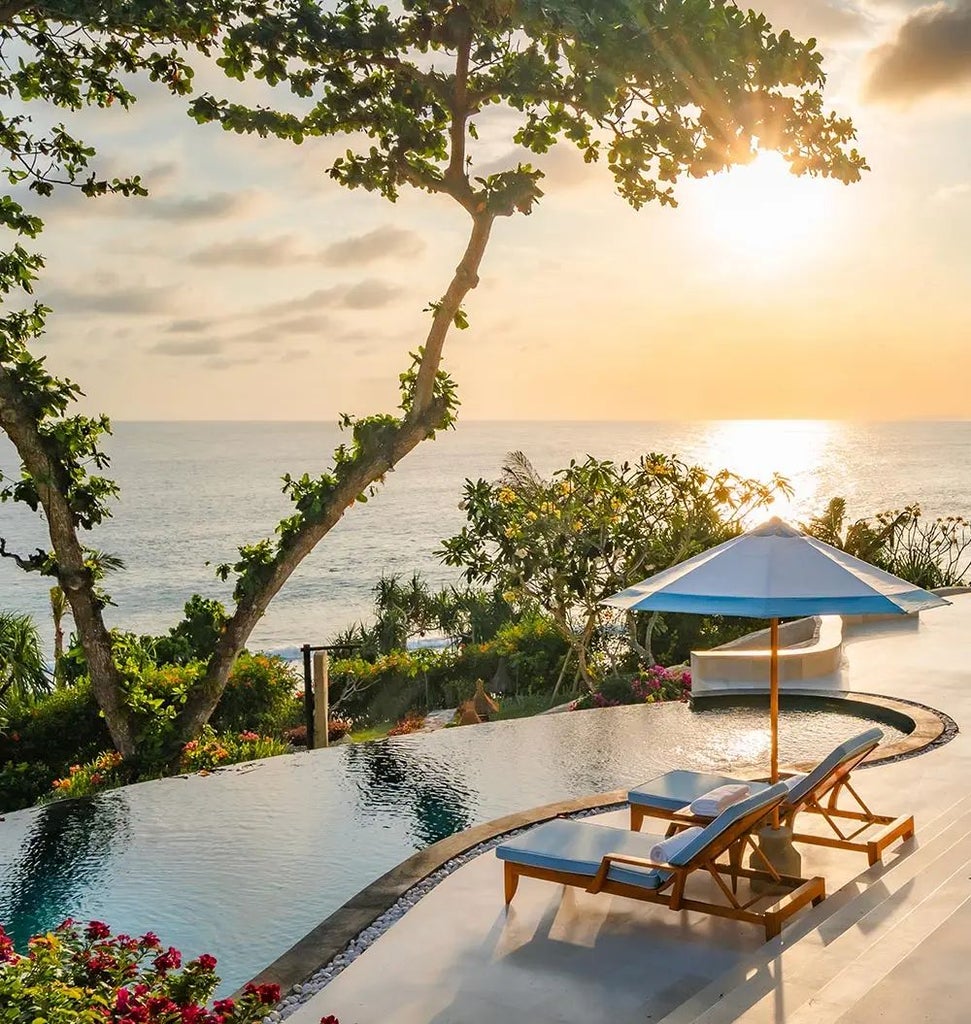 Luxurious open-air bedroom at NIHI Sumba's Kasambi Estate, featuring wooden floors, traditional thatched roof, and panoramic views of lush Indonesian landscape