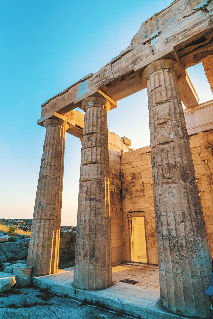 Ancient Greek temple Parthenon illuminated at dusk against dramatic pink sky, perched atop Acropolis hill overlooking Athens cityscape