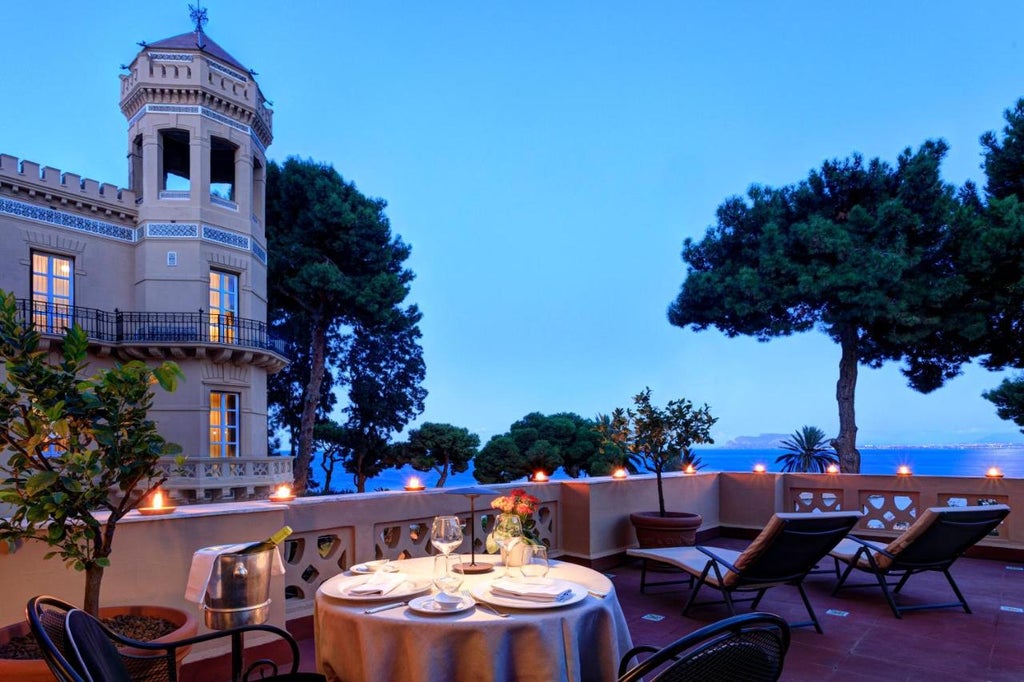 Elegant Italian villa hotel with ornate stone balconies, manicured gardens, and Mediterranean architecture overlooking the sea at sunset