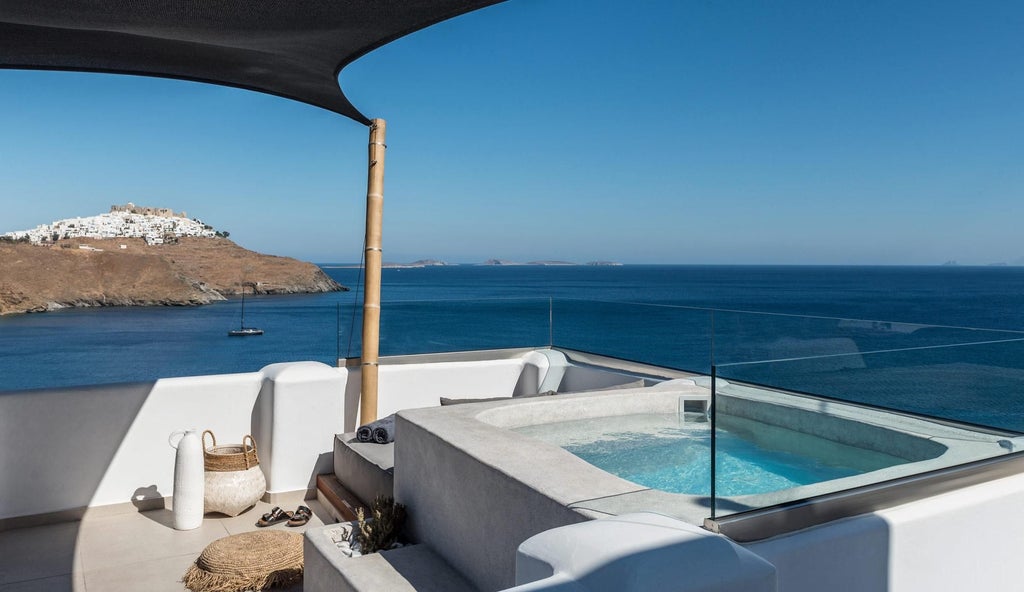 Elegant white-washed Cycladic suite with blue shutters overlooking azure Aegean waters, featuring a luxurious private balcony with panoramic Greek island scenery