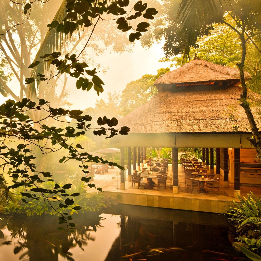 Elegant infinity pool overlooking lush Balinese jungle at COMO Uma Ubud resort, with traditional pavilion and stone details at sunset