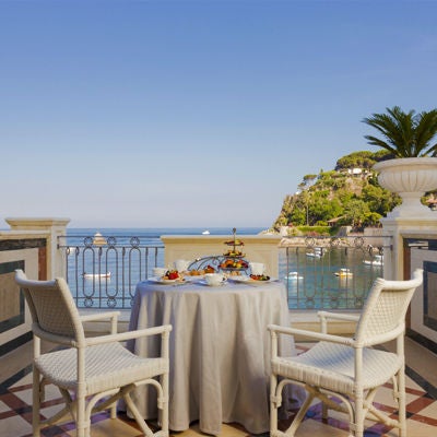 Elegant luxury hotel suite with a private balcony overlooking the Mediterranean Sea, featuring classic Italian decor and sun loungers.