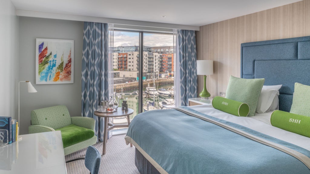 Luxurious deluxe hotel room with expansive marina view, featuring modern decor, plush bedding, and floor-to-ceiling windows overlooking Southampton's waterfront.