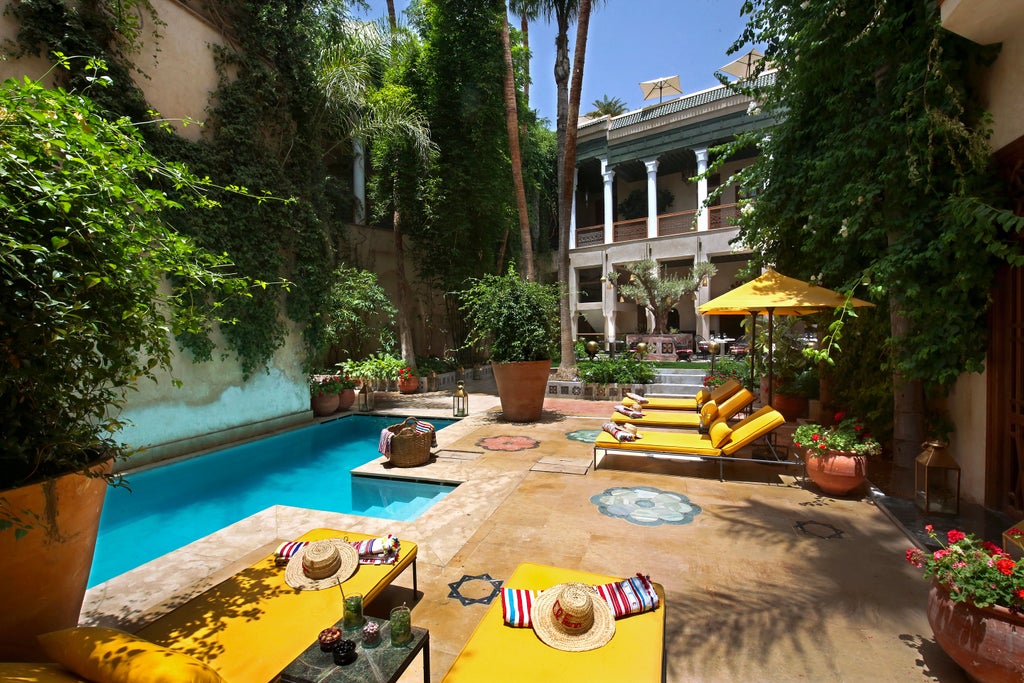 Luxurious Moroccan riad interior with vibrant pink walls, traditional archways, ornate hanging lanterns and plush lounge seating near pool